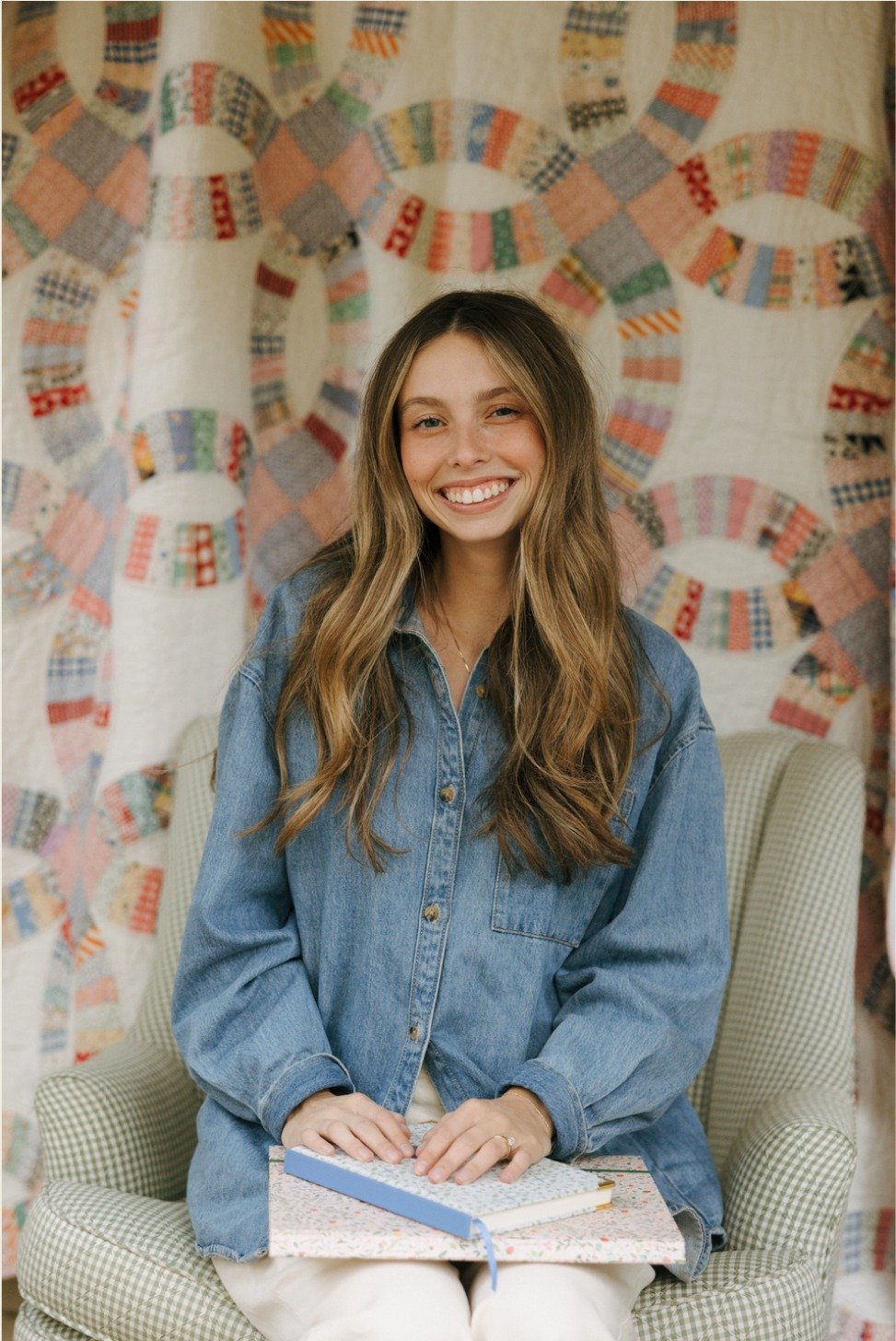 Founder of Woven Designs seated in front of a patchwork quilt, holding a planning notebook