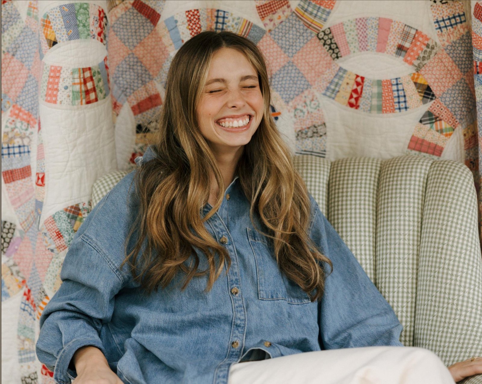 Founder of Woven Designs laughing, seated in front of a vintage patchwork quilt